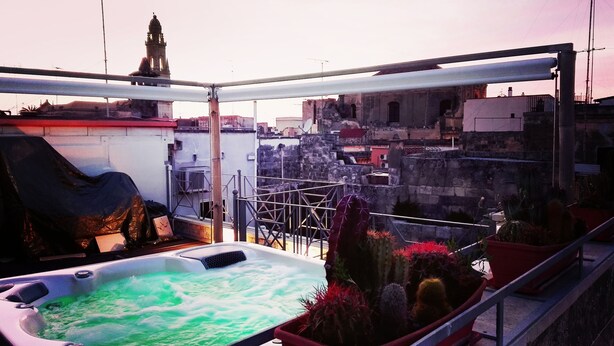 Terraço no telhado com hidromassagem, plantas em vasos e vista para a cidade, incluindo um campanário.