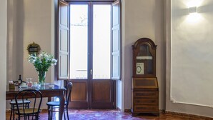Quarto com piso de mármore, uma cama, uma escrivaninha com cadeiras, um espelho e uma porta que dá para o exterior.