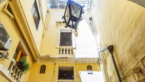 Uma rua estreita com entrada de edifício, uma pequena varanda e plantas em vasos.