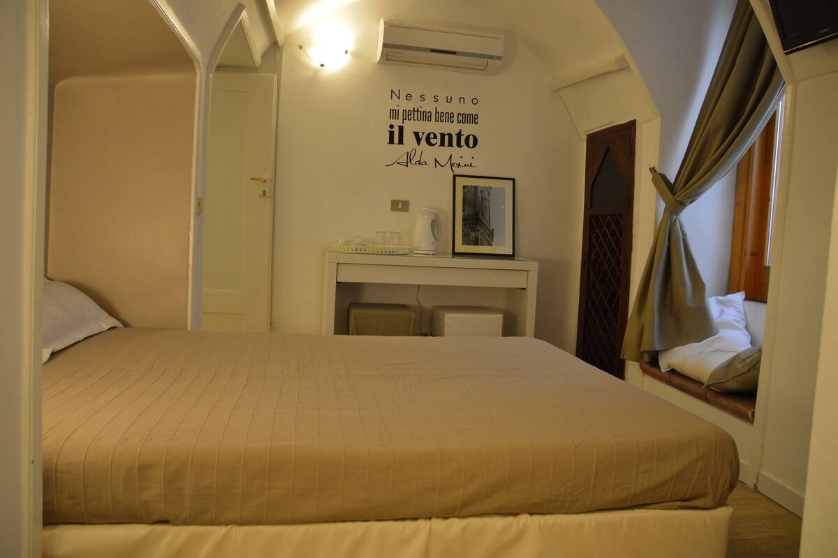 A bedroom with a bed, a desk with a chair, a framed picture, and a wall with a quote.