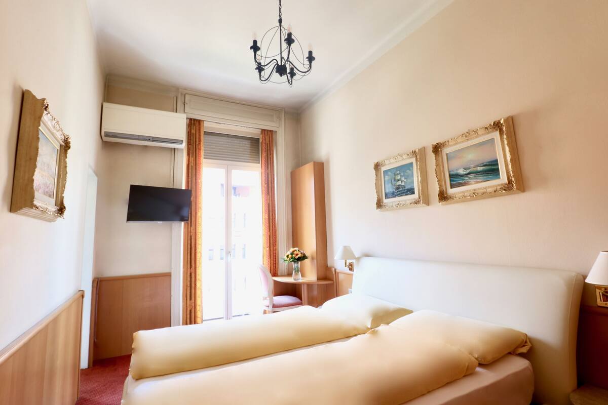 Een hotelkamer met een bed, een televisie, een bureau, een stoel en twee ingelijste foto’s aan de muur.
