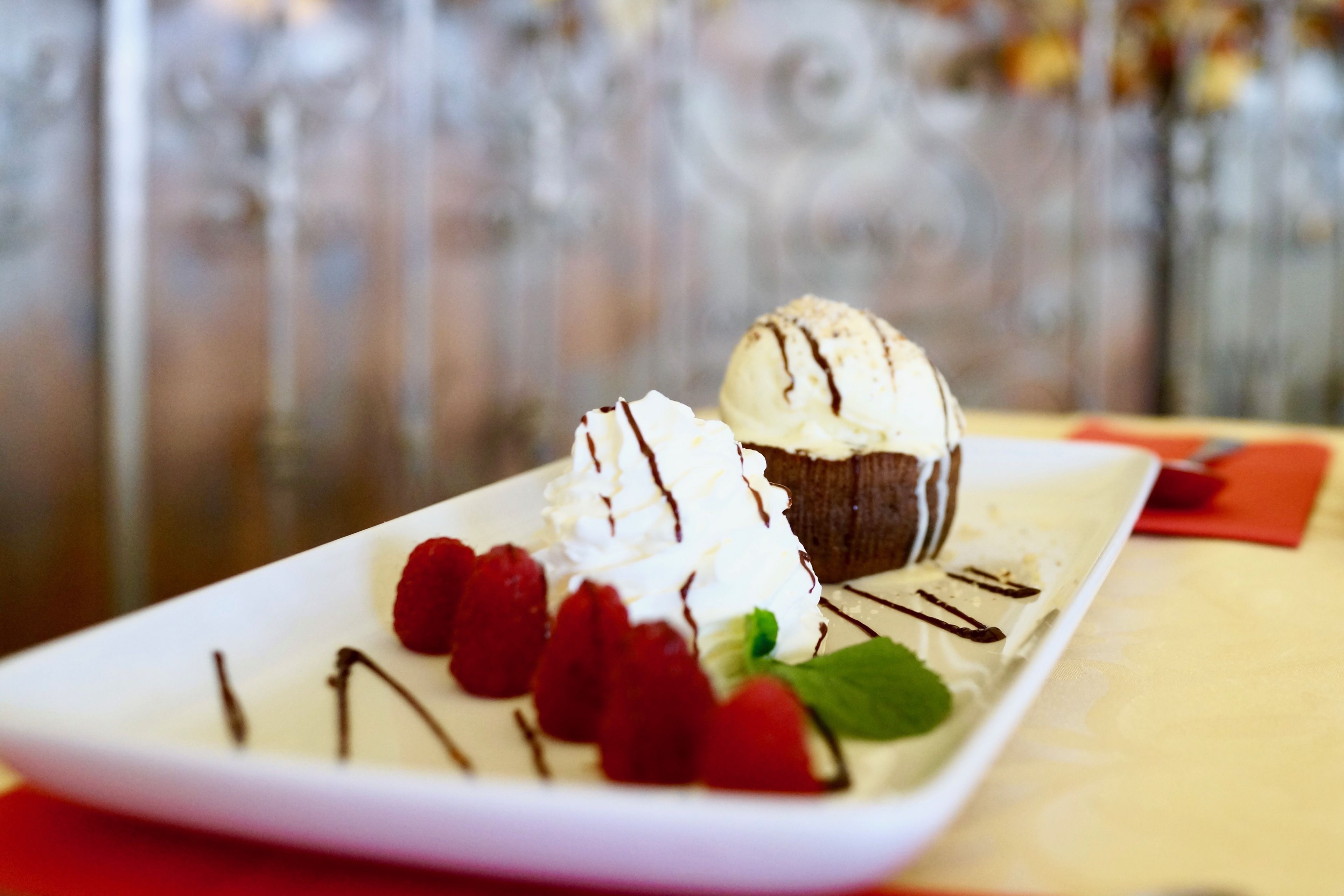 Un plato de postre con helado y frambuesas sobre una vajilla blanca.
