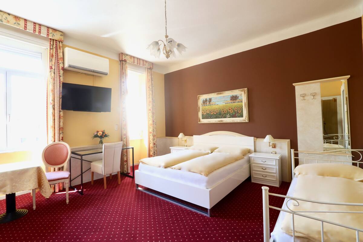 Een hotelkamer met een bed, nachtkastjes, een bureau met stoel, een televisie en een raam met gordijnen.