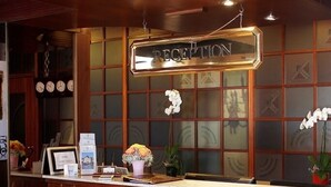 A reception desk with a sign that reads "RECEPTION," a clock, and a vase with flowers. - Hotel Victoria au Lac (Paradiso)