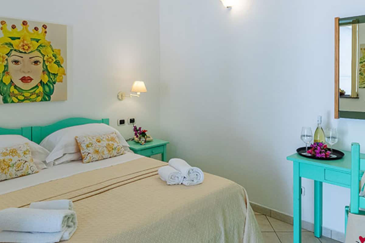 Una habitación de hotel con una cama, una mesita de noche, un espejo y una pequeña mesa con una bandeja de flores y vasos.