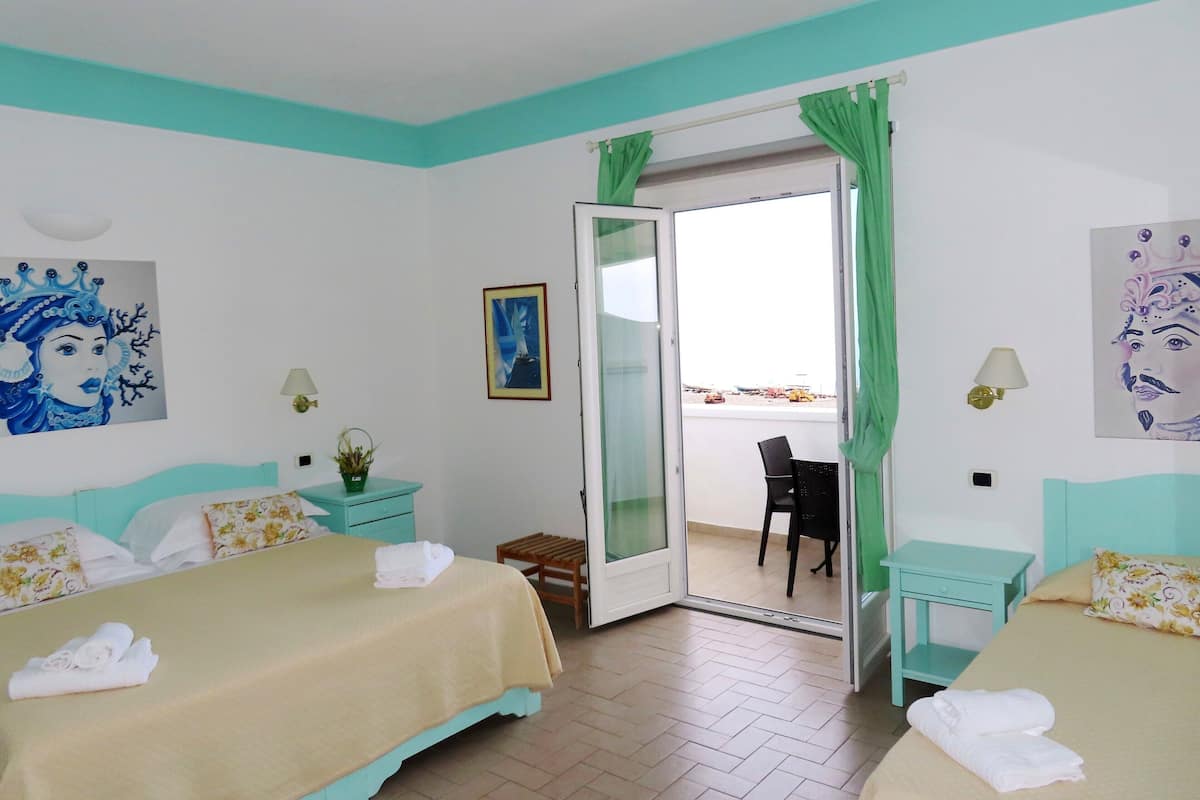 Una habitación de hotel con dos camas, un balcón y vistas, y obras de arte en las paredes.