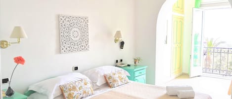 Habitación de hotel luminosa con cama, mesitas de noche, un adorno en la pared y vistas al balcón exterior.