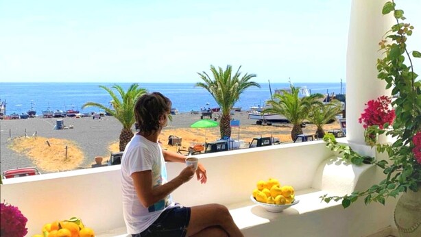 A person sitting on a balcony with a view of the beach and the sea.