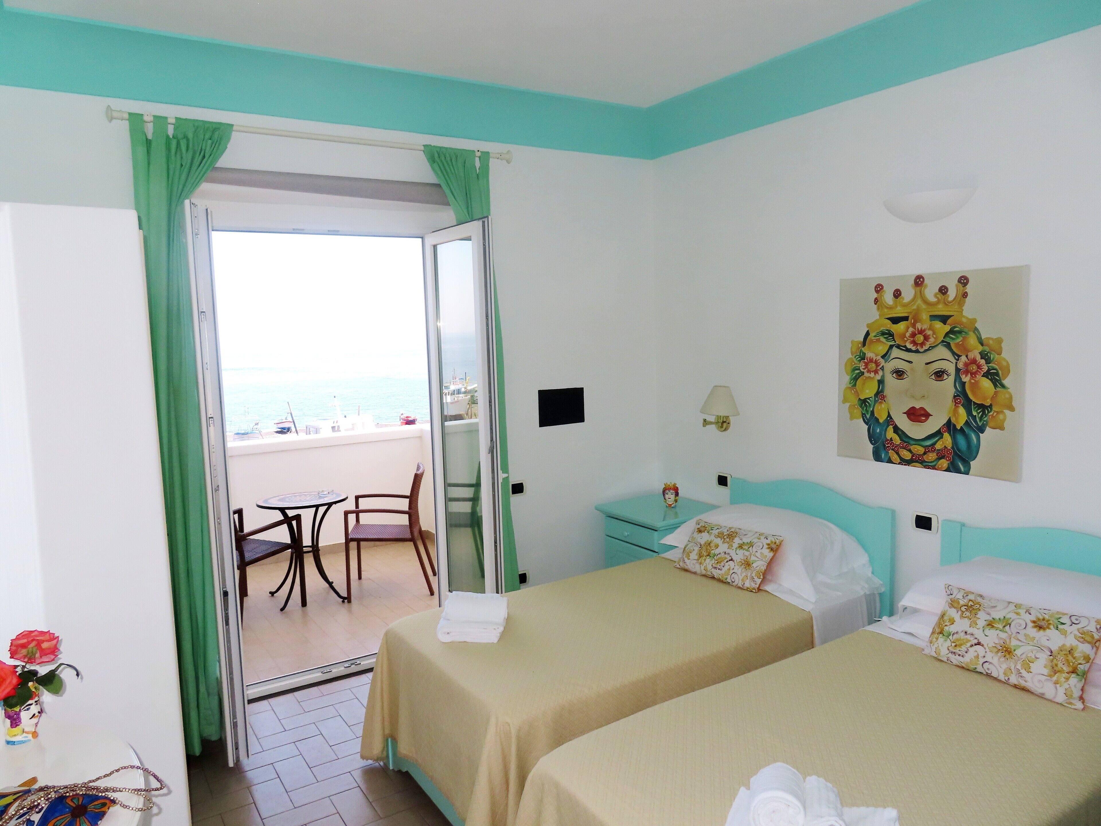 Une chambre d’hôtel avec deux lits, un balcon donnant sur la mer et un tableau accroché au mur.