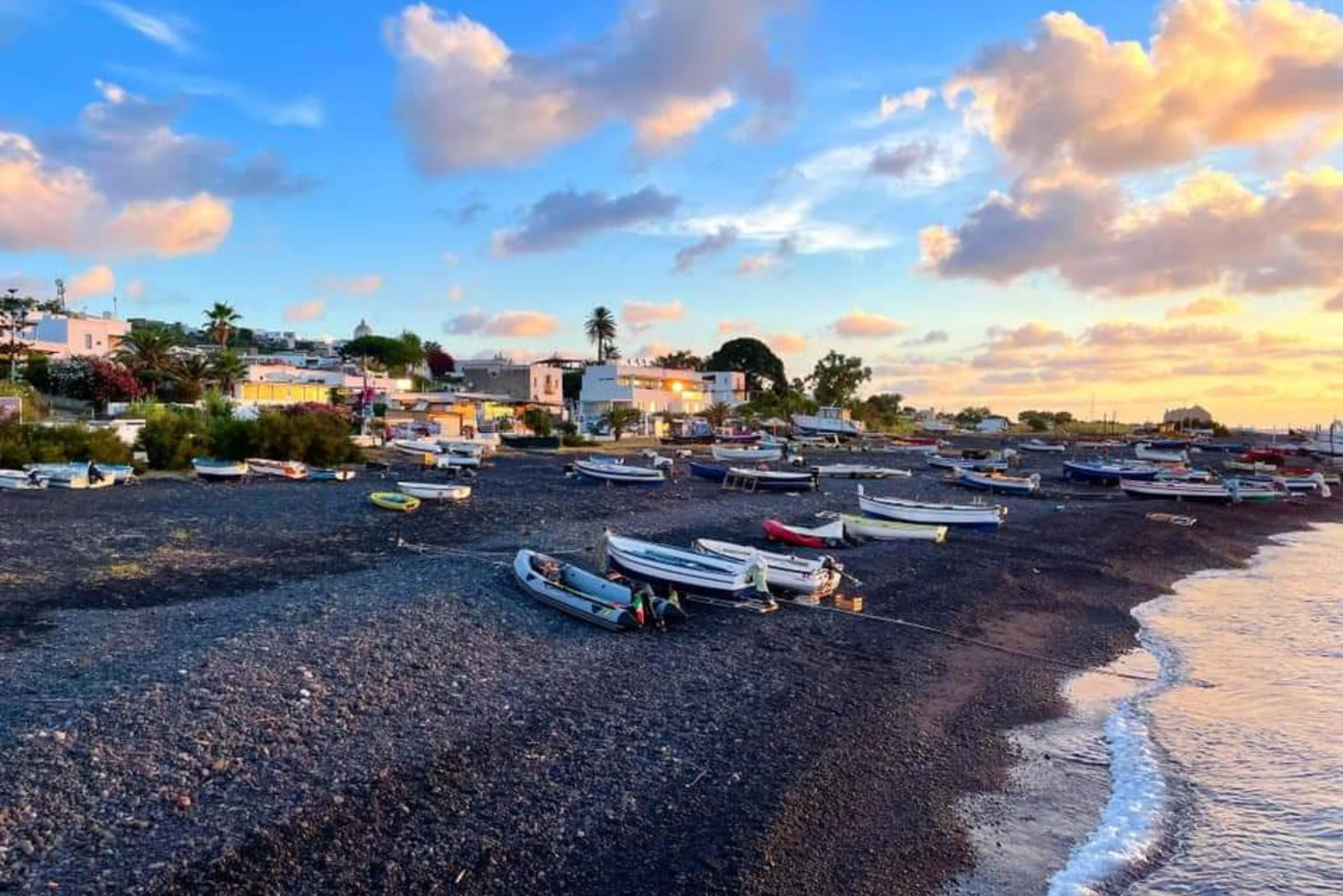 Una playa de adoquines con numerosos barcos amarrados, edificios al fondo y un cielo despejado.