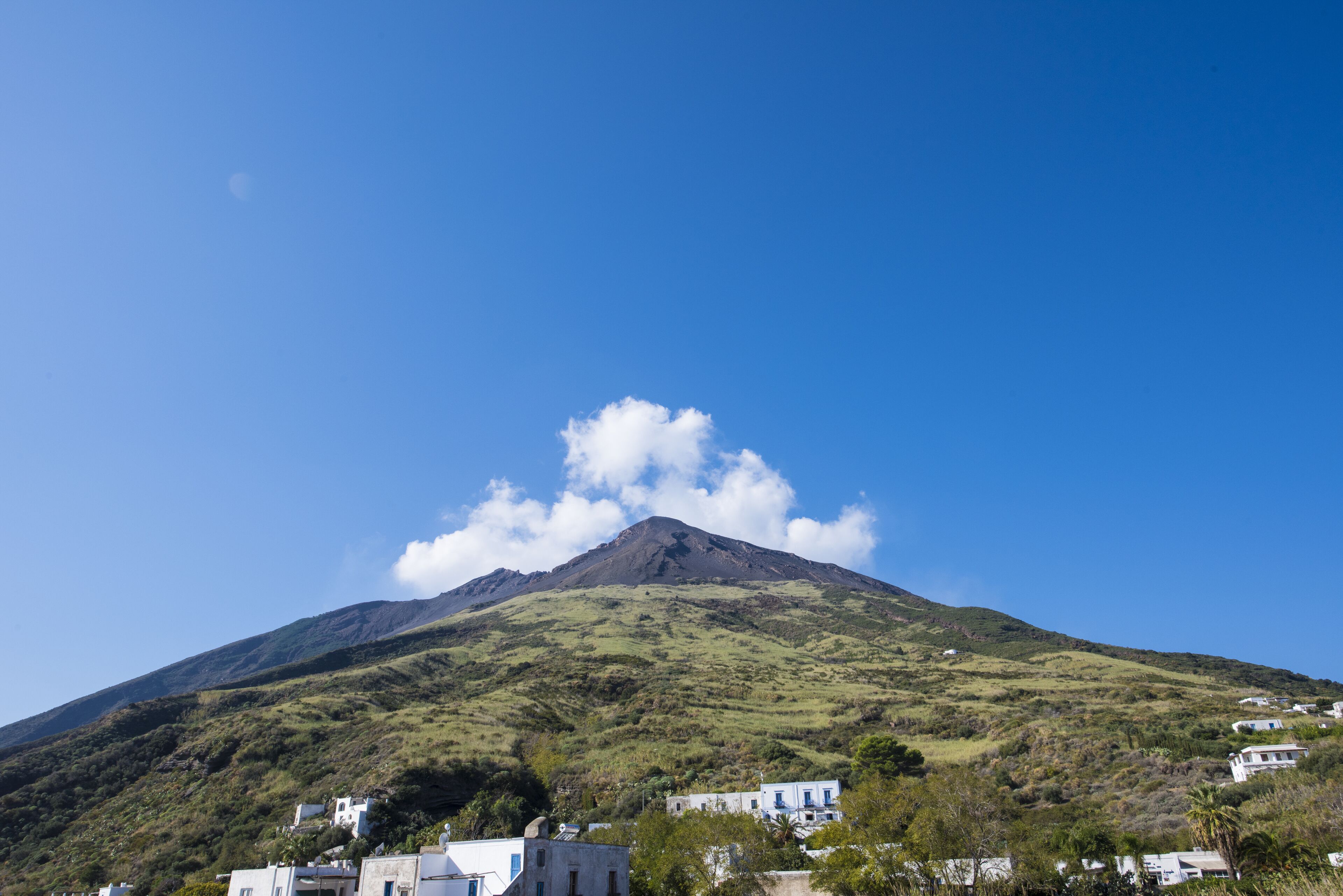A mountain with a small cloud, surrounded by buildings.