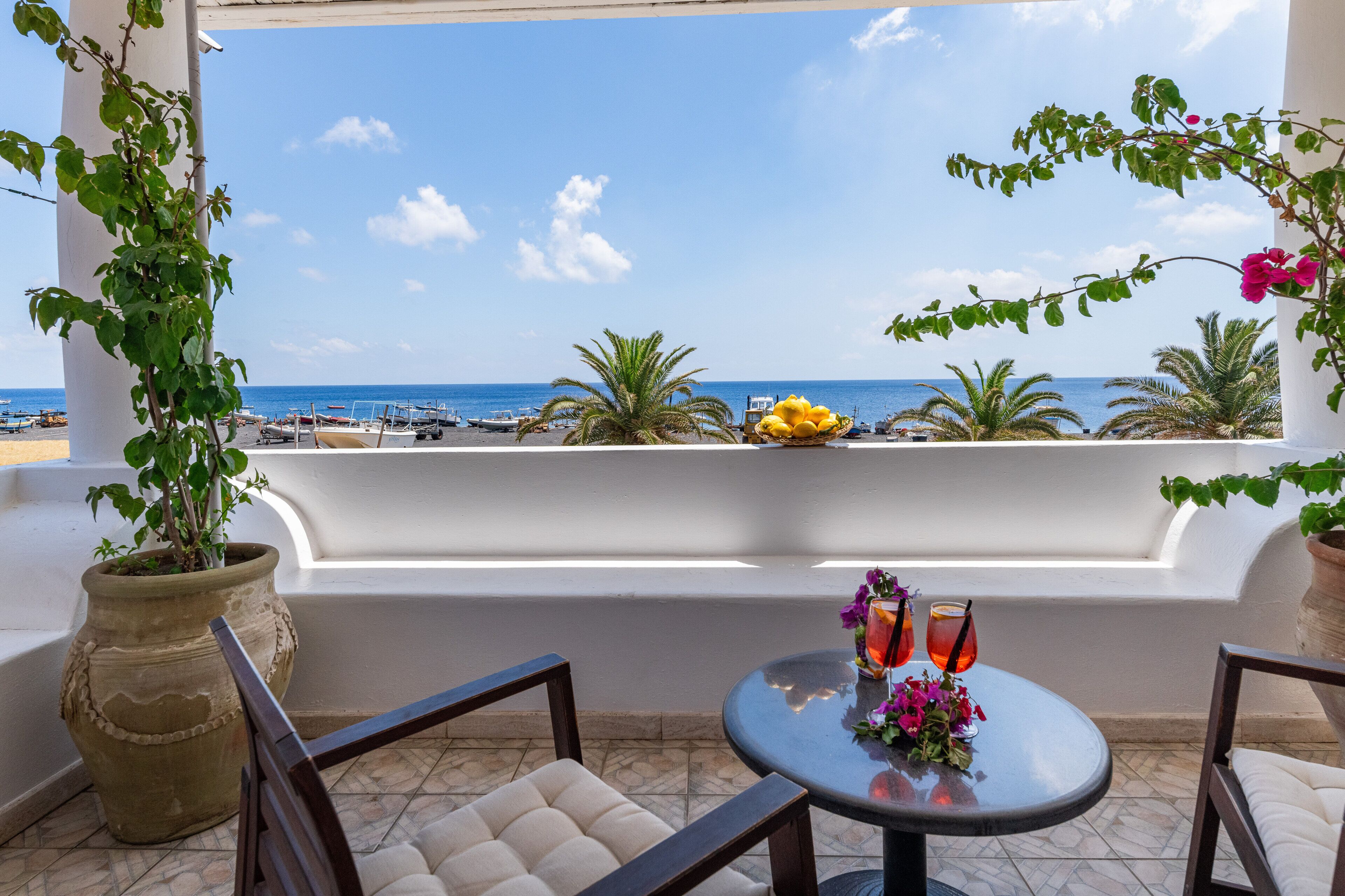Un balcone con vista sul mare, un tavolo con bevande e piante in vaso.