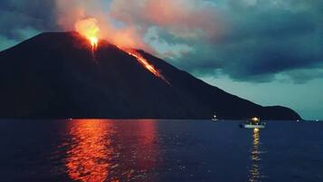 A volcano erupting at night with lava flowing down its side, reflecting on the water.
