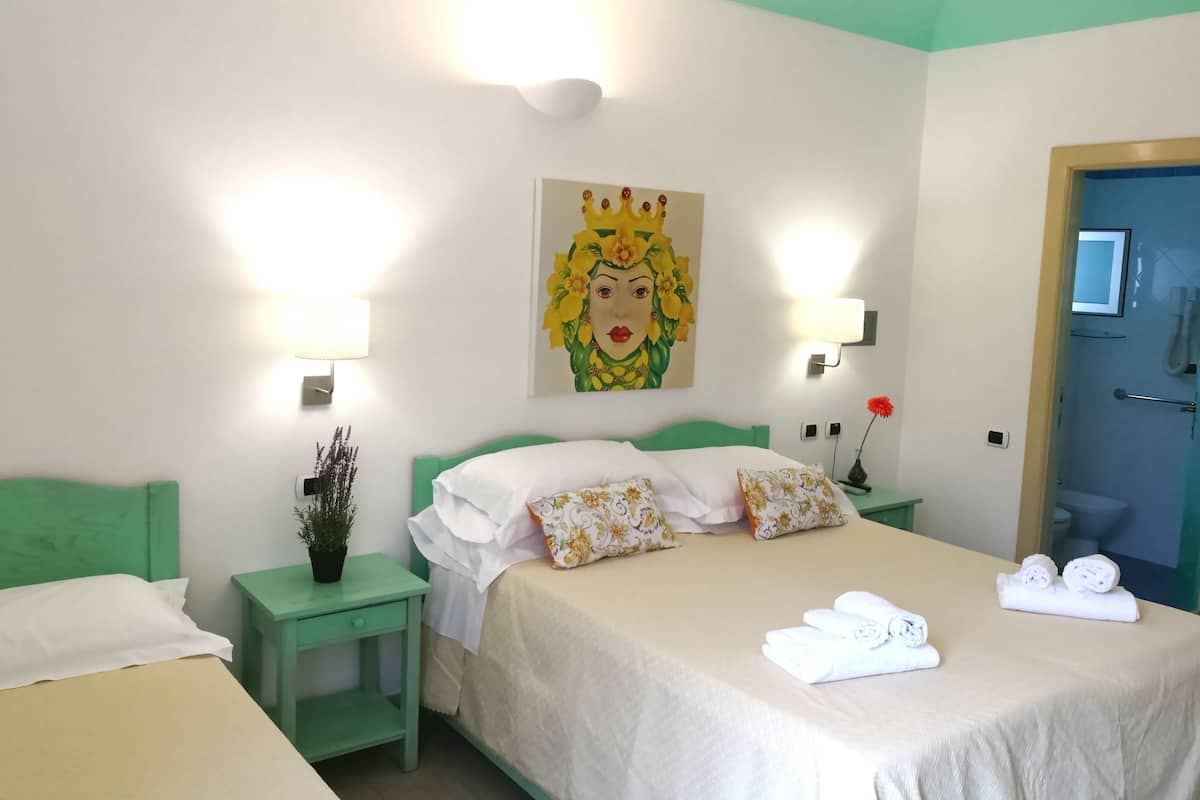 Habitación de hotel con cama, dos mesitas de noche, un florero con flores y toallas sobre la cama.