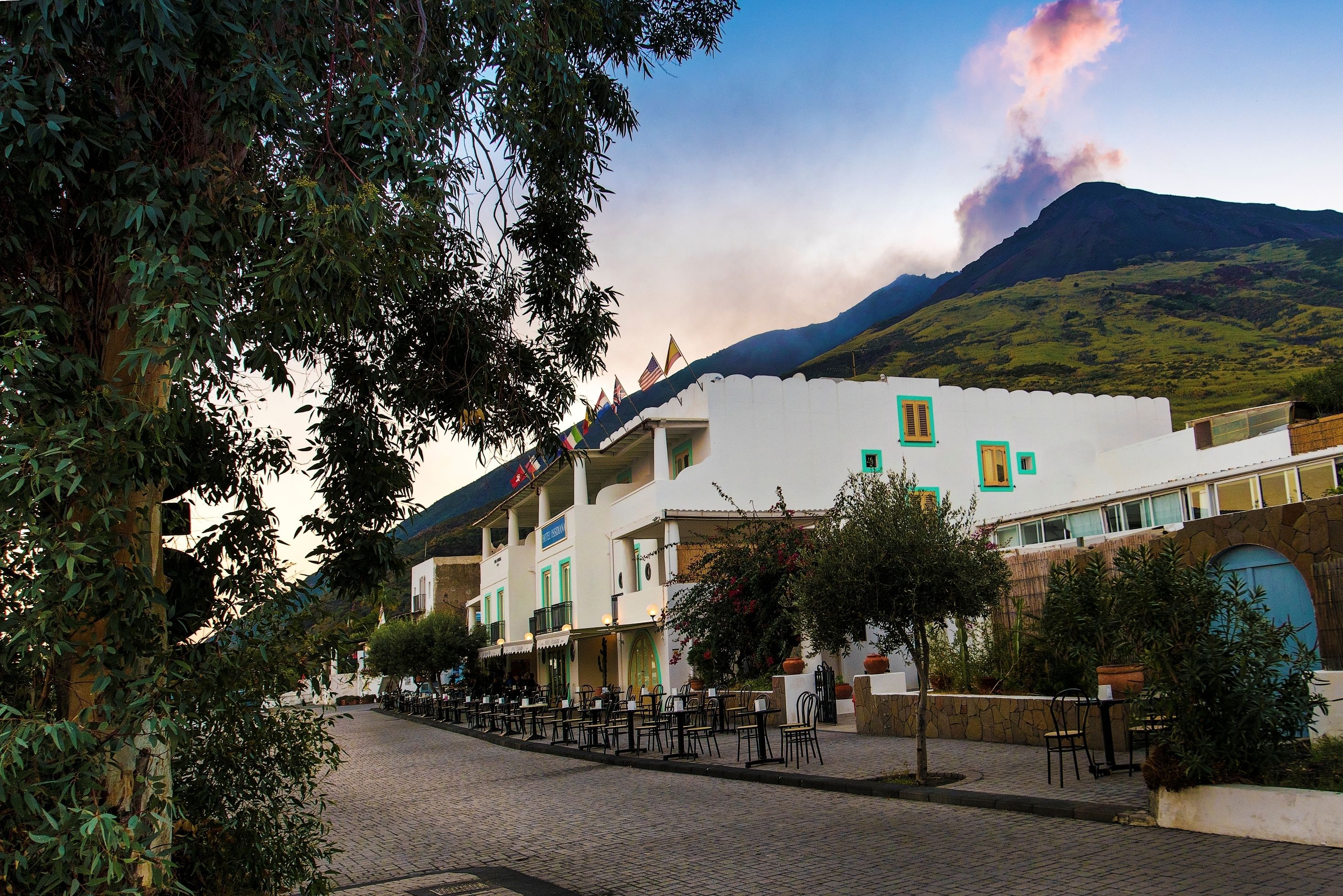 A cobblestone street lined with buildings, outdoor seating, and a mountain in the background.