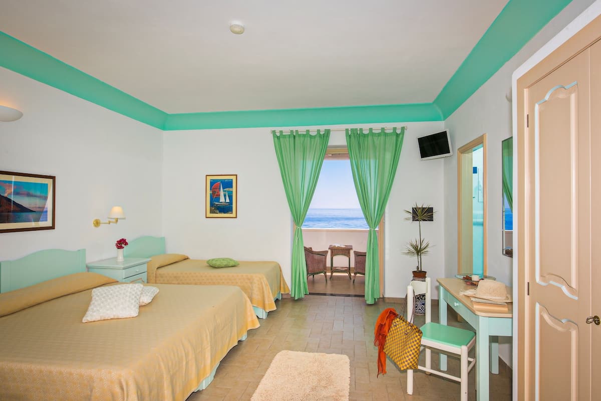 Habitación de hotel con dos camas, un escritorio, una silla, un televisor y vista al mar.