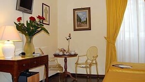 A hotel room with a bed, a desk with a lamp, a vase with flowers, a chair, and a television on the wall. - Residenza Giotto (Florence)