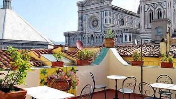 A rooftop terrace with tables and chairs, potted plants, and a view of a historic building with intricate architecture. - Residenza Giotto (Florence)