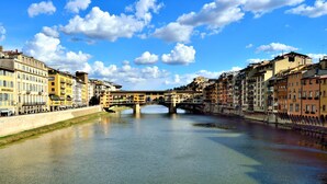A river with a bridge, surrounded by multi-story buildings with balconies. - Residenza Giotto (Florence)