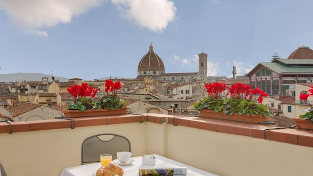 Un balcon avec une table dressée pour le petit-déjeuner, offrant une vue sur un paysage urbain avec des bâtiments historiques et un imposant dôme.