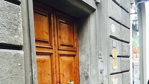 Une porte à deux battants en bois, dotée de poignées en laiton, intégrée dans un bâtiment en béton dont la façade est en pierre.
