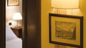 Una camera d'hotel con una porta in legno, un quadro appeso al muro e una lampada su un comodino.