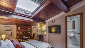 Une chambre dotée d’une lucarne, d’une télévision, d’une salle de bain avec douche et d’un bureau avec des livres et une lampe.