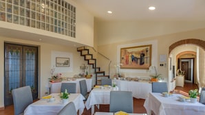 Une salle à manger avec plusieurs tables dressées pour les repas, un escalier et un tableau accroché au mur.