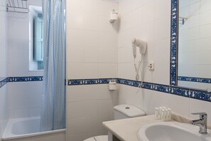 A bathroom with a bathtub, a toilet, a sink, and a hairdryer mounted on the wall. - Apartamentos Suites Santa Cruz (Seville)