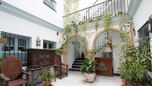 A spacious interior with a staircase, wooden furniture, and potted plants. - Apartamentos Suites Santa Cruz (Seville)