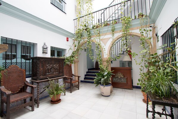 A spacious interior with a staircase, wooden furniture, and potted plants. - Apartamentos Suites Santa Cruz (Seville)