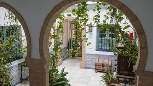 An arched corridor with hanging plants, tiled flooring, and a bench. - Apartamentos Suites Santa Cruz (Seville)