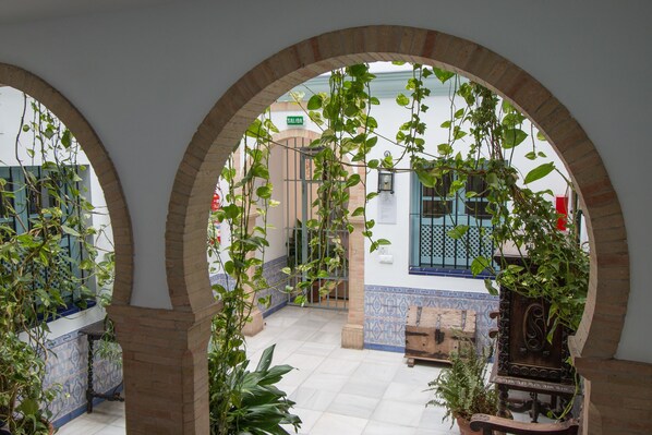 An arched corridor with hanging plants, tiled flooring, and a bench. - Apartamentos Suites Santa Cruz (Seville)