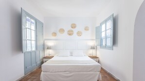 A bedroom with a large bed, two bedside tables with lamps, a wardrobe, and a wall with circular decorations. - Apartamentos Suites Santa Cruz (Seville)
