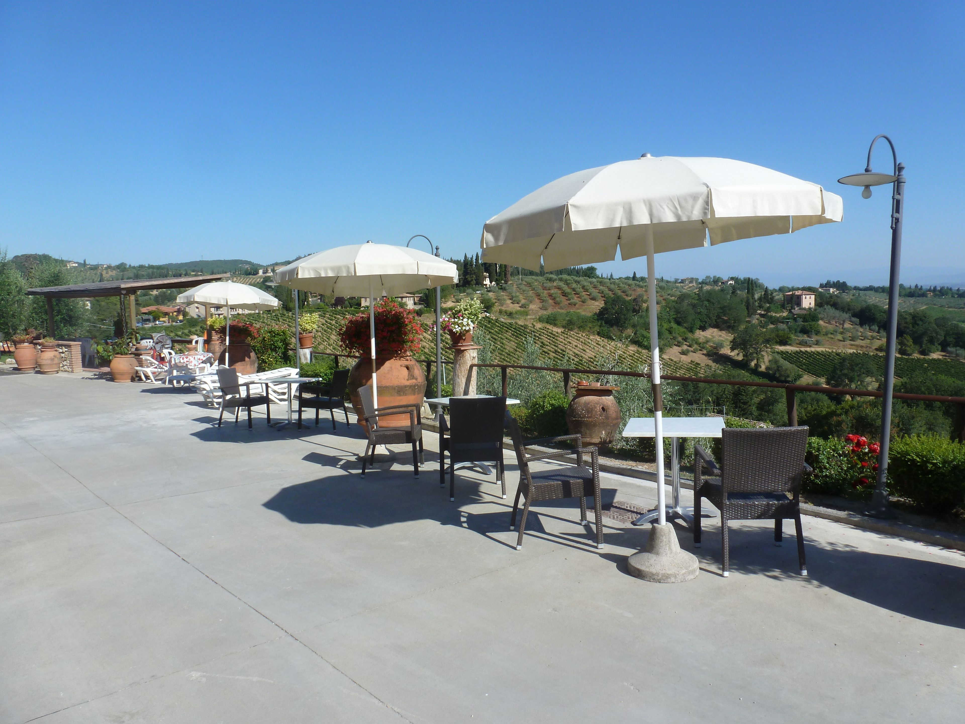 Patio esterno con tavoli e sedie sotto ombrelloni, con vista su un vigneto.