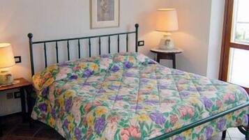 Un letto con una coperta a fiori, due lampade ai lati, un quadro appeso al muro e una finestra con vista.