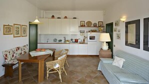 Een ruimtelijk ingerichte leefruimte met kitchenette, een eethoek met tafel en stoelen, een bank en een lamp.