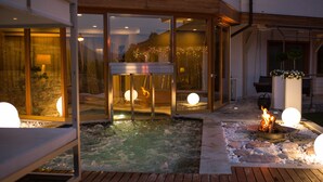Un espacio exterior moderno con piscina climatizada, una chimenea y puertas de vidrio que dan a un edificio.