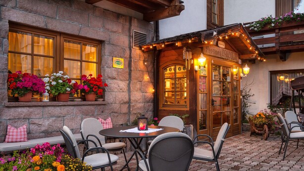 An outdoor seating area with stone walls, potted flowers, and a wooden building entrance.