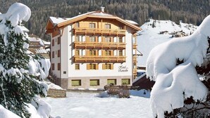 A multi-story hotel with a traditional Alpine architectural style, surrounded by snow-covered mountains and trees.
