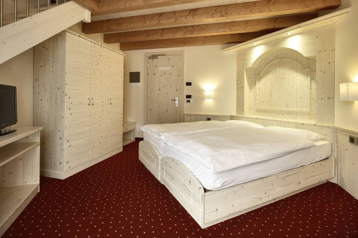 A bedroom with a wooden bed, a wardrobe, a television, and a mirror.