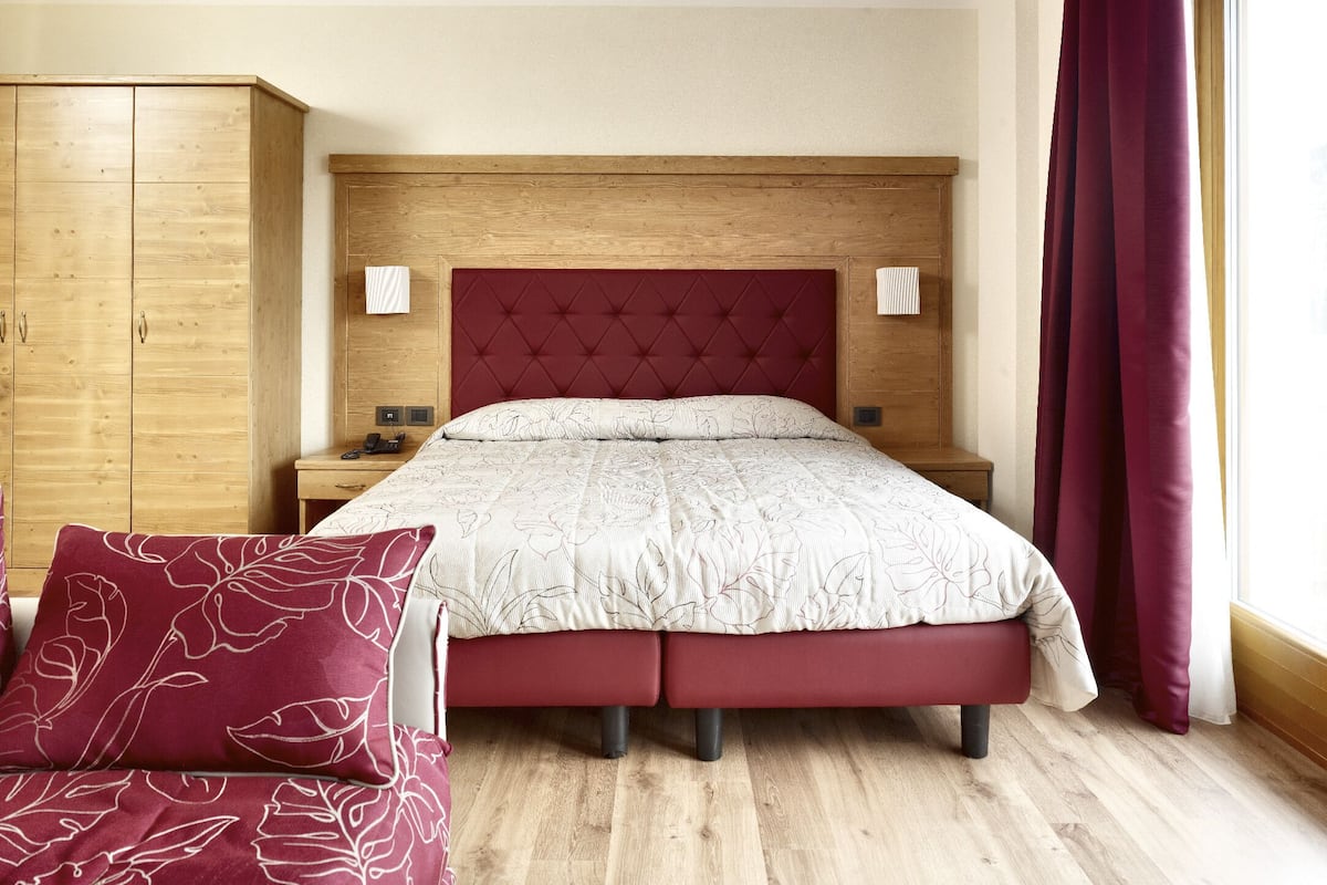 A bedroom with a wooden headboard, a bed with floral bedding, a nightstand, a wardrobe, and a window with curtains.