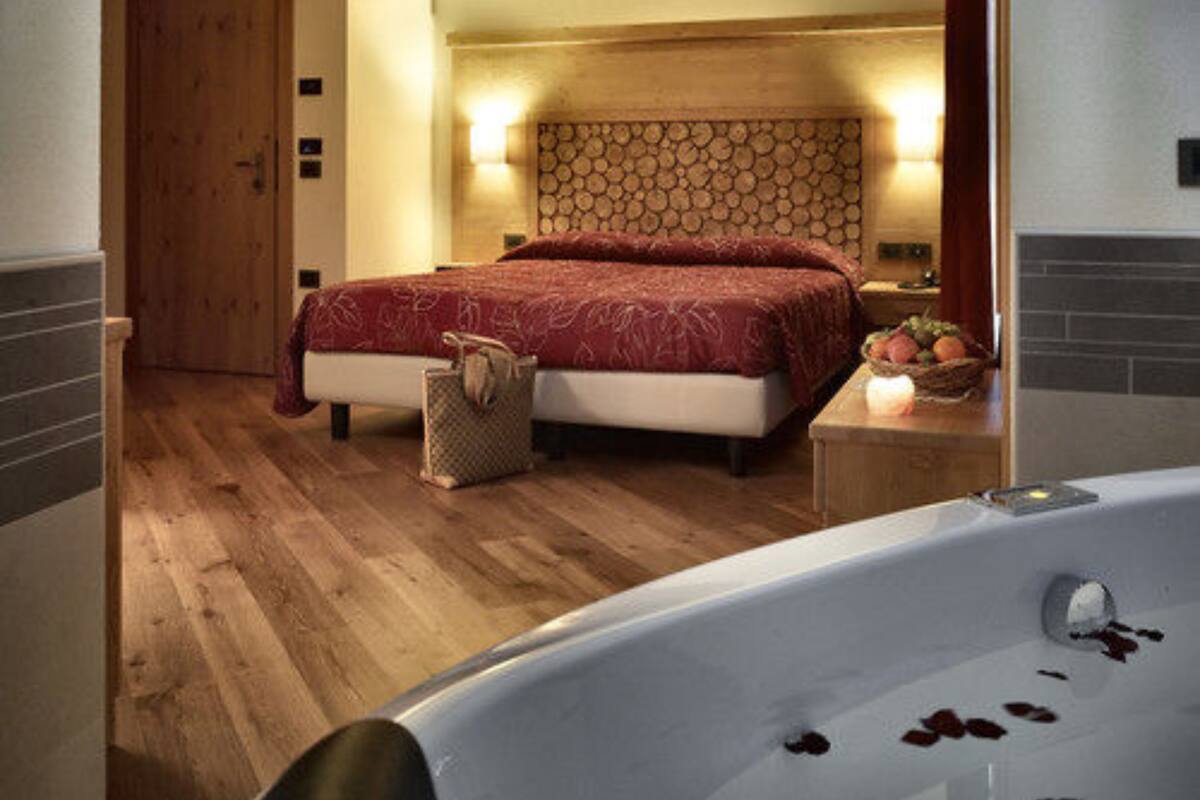 A bedroom with a wooden floor, a bed with a red bedspread, a nightstand with a basket, and a bathroom with a bathtub.