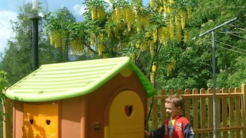 Cozy playhouse with a green roof and yellow door, surrounded by a grassy area and a wooden fence.