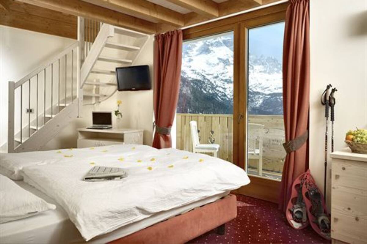 A bedroom with a bed, a desk, a chair, a TV, and a view of mountains.