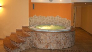 A circular hot tub with mosaic stone steps leading up to it, set against an orange wall with recessed lighting. - Stella delle Alpi (Ronzone)
