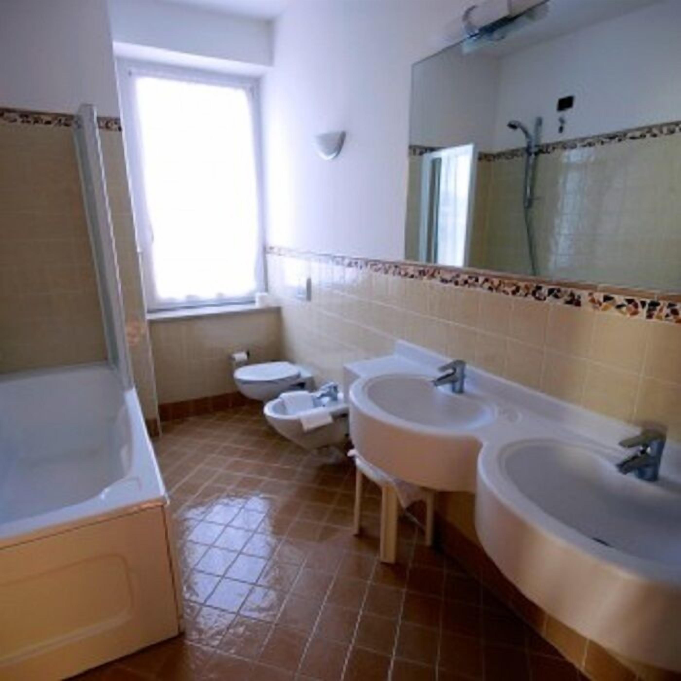 Un baño con bañera, dos lavamanos, un inodoro y una ventana.