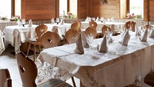A dining area with wooden walls, tables set with white tablecloths and heart-shaped cutouts, and hanging pendant lights. - Stella delle Alpi (Ronzone)