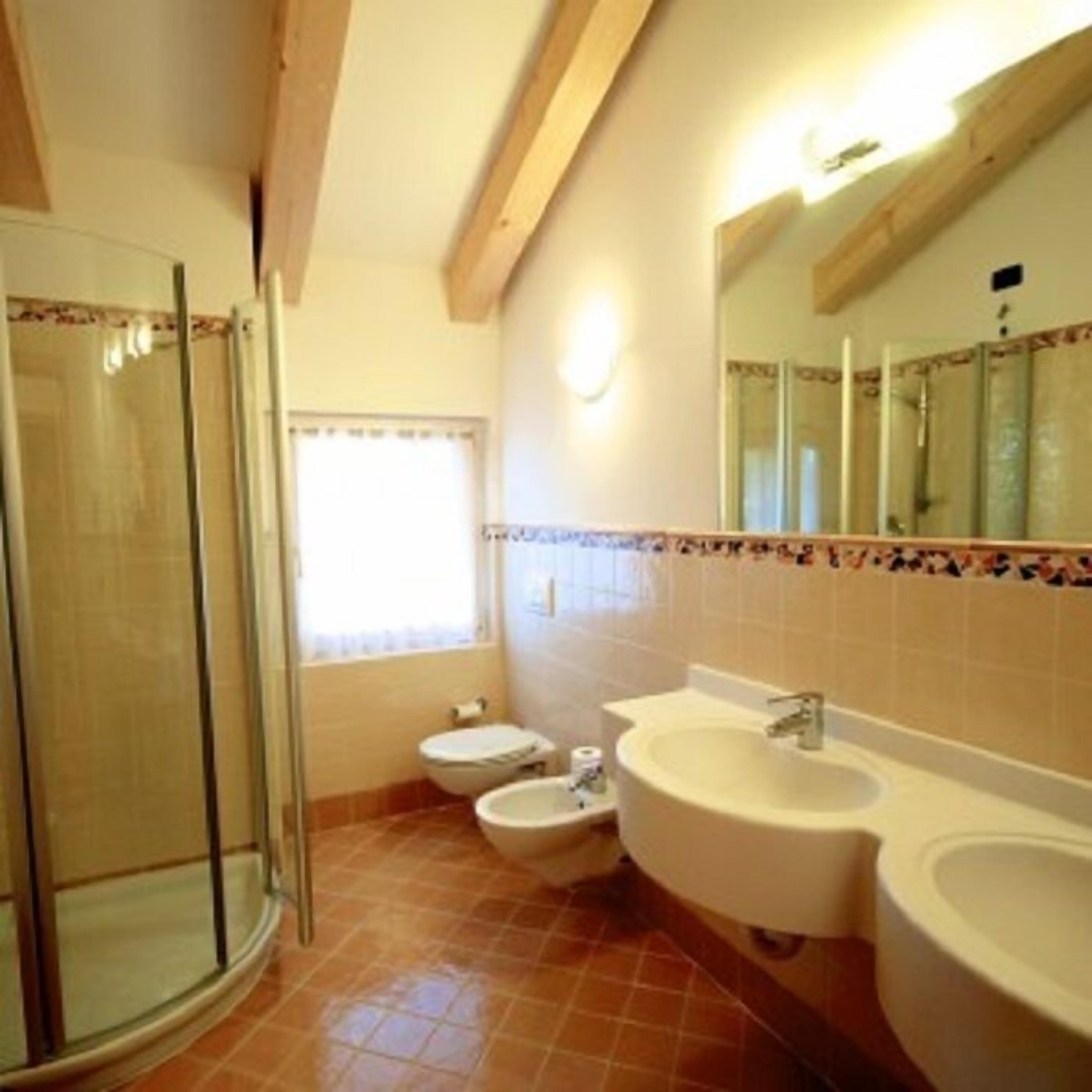 A bathroom with a glass shower enclosure, two toilets, a sink, and a mirror.