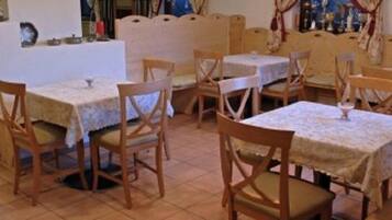 A dining area with multiple tables and chairs, a tiled floor, and hanging pendant lights.